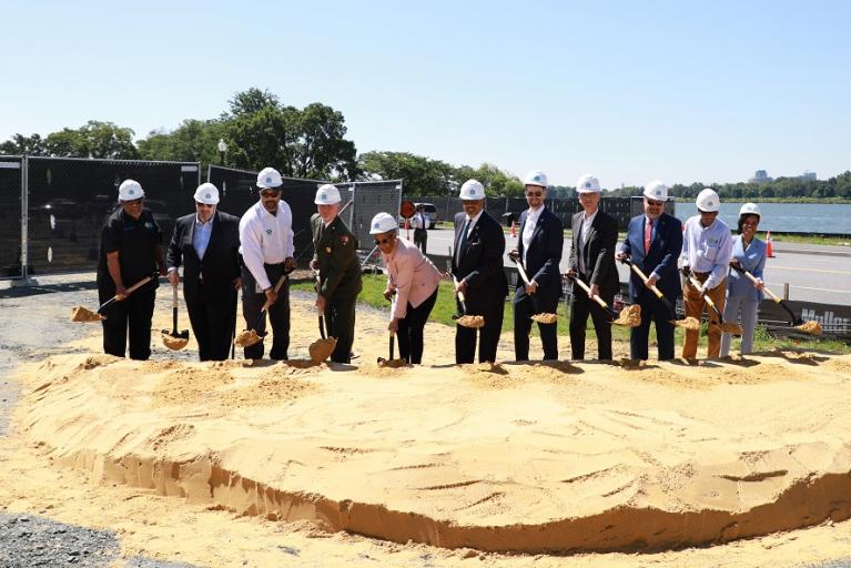 Speakers and other VIPs in hardhats lift dirt on their shovels during the ceremonial groundbreaking