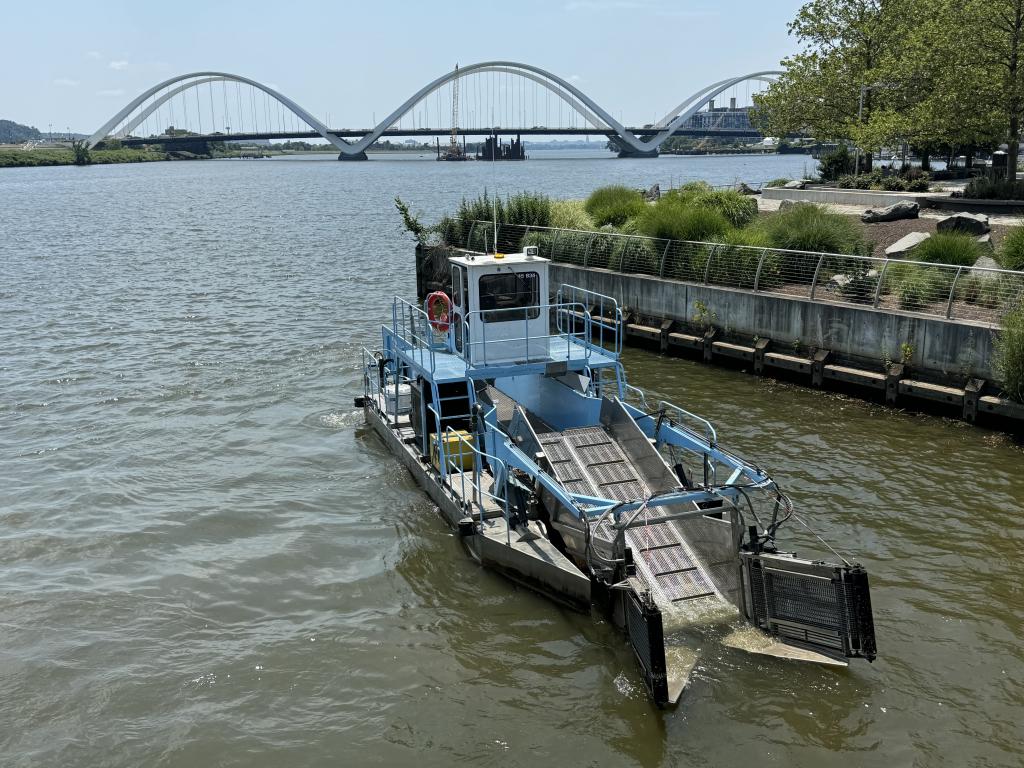 One of DC Water's skimmer boats on the Anacostia River with the Frederick Douglass Bridge in the background.